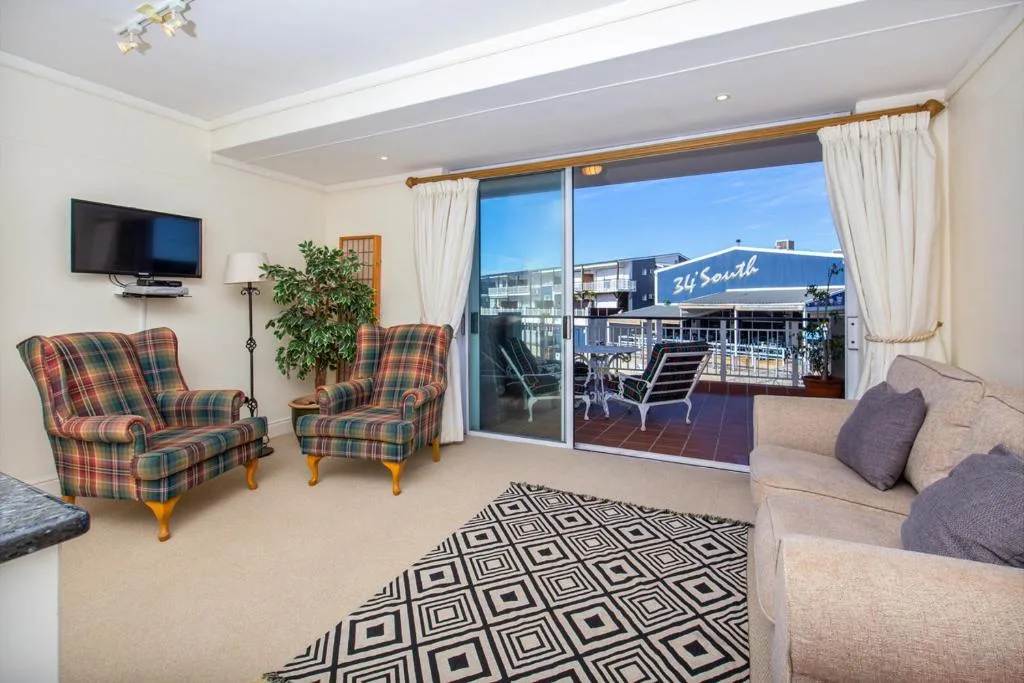 Bright lounge with plaid armchairs, sofa, TV, and waterfront views through sliding doors