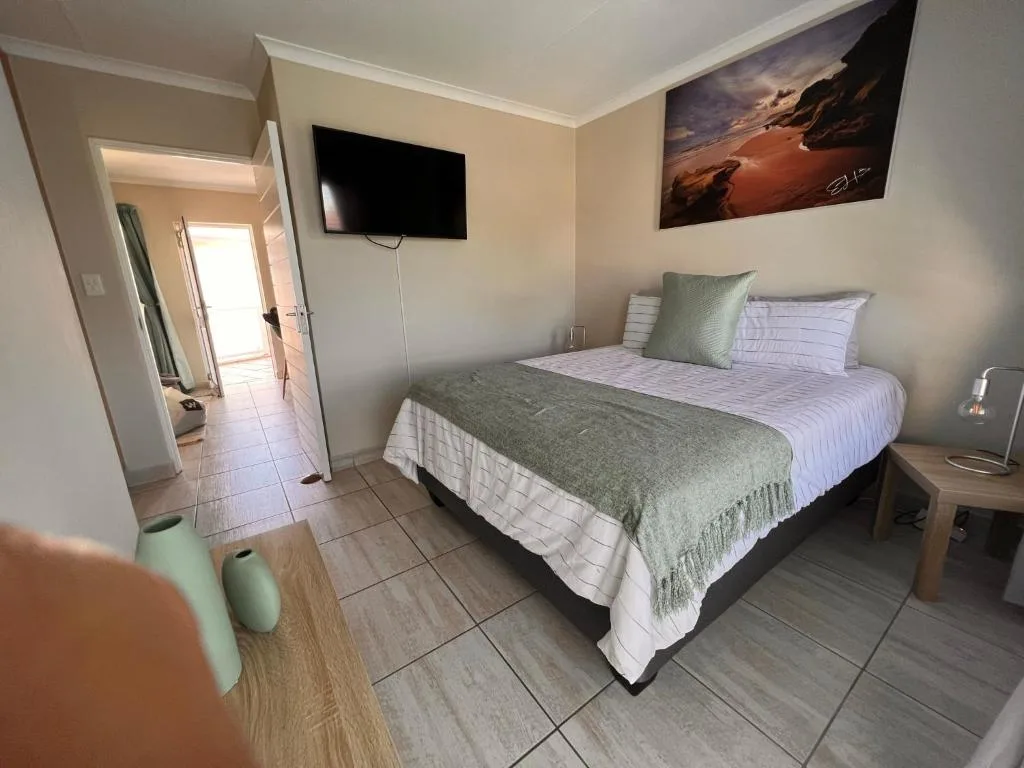 Bright bedroom with queen bed, TV, and coastal landscape wall art
