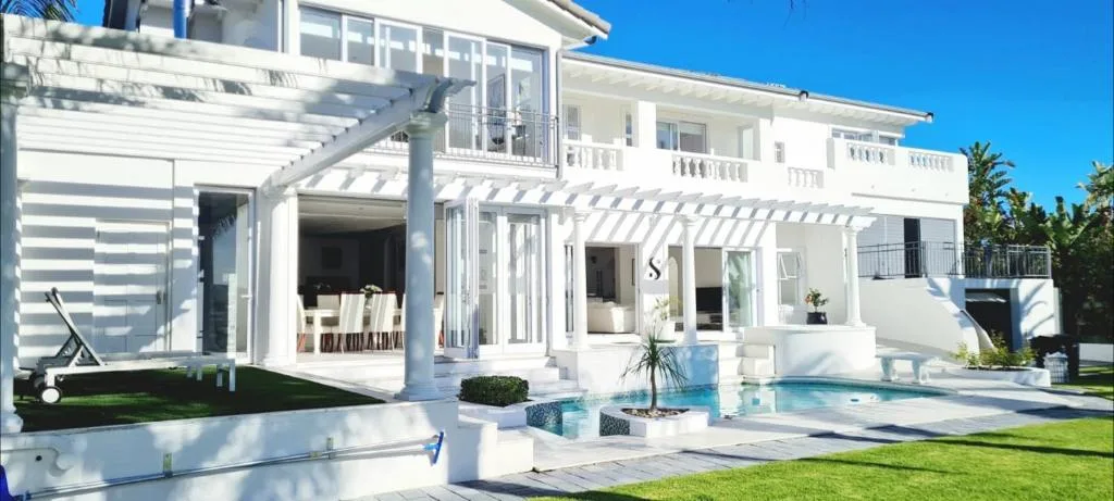 Modern white holiday home with pool, manicured lawn, and deck areas