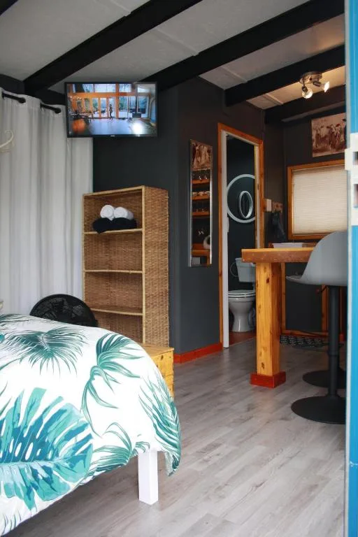Compact studio bedroom with tropical bedding, wicker storage, and work desk area