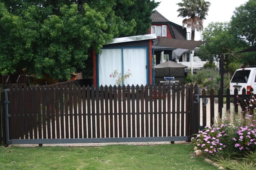Colorful cottage with black gate, lush gardens, and mature trees surrounding property