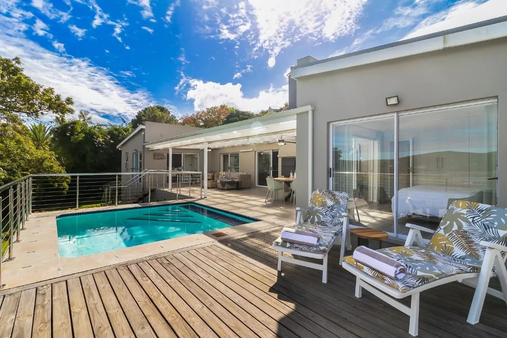 Modern villa with turquoise swimming pool, wooden deck, and lounge chairs
