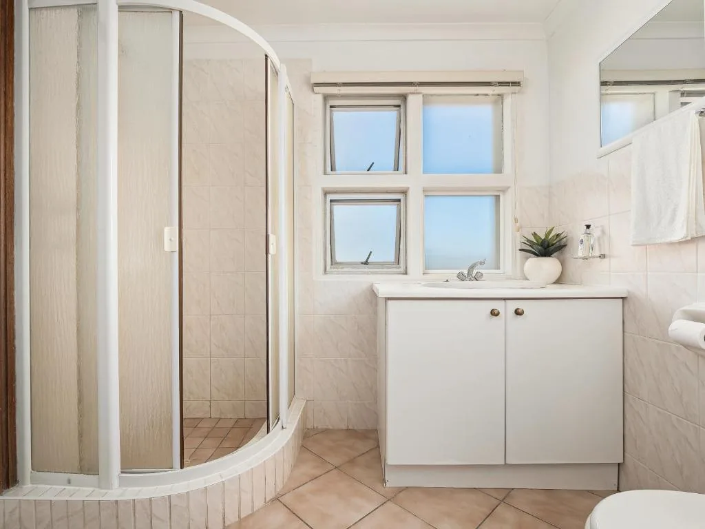 Bright bathroom with curved shower enclosure, white vanity, and window views