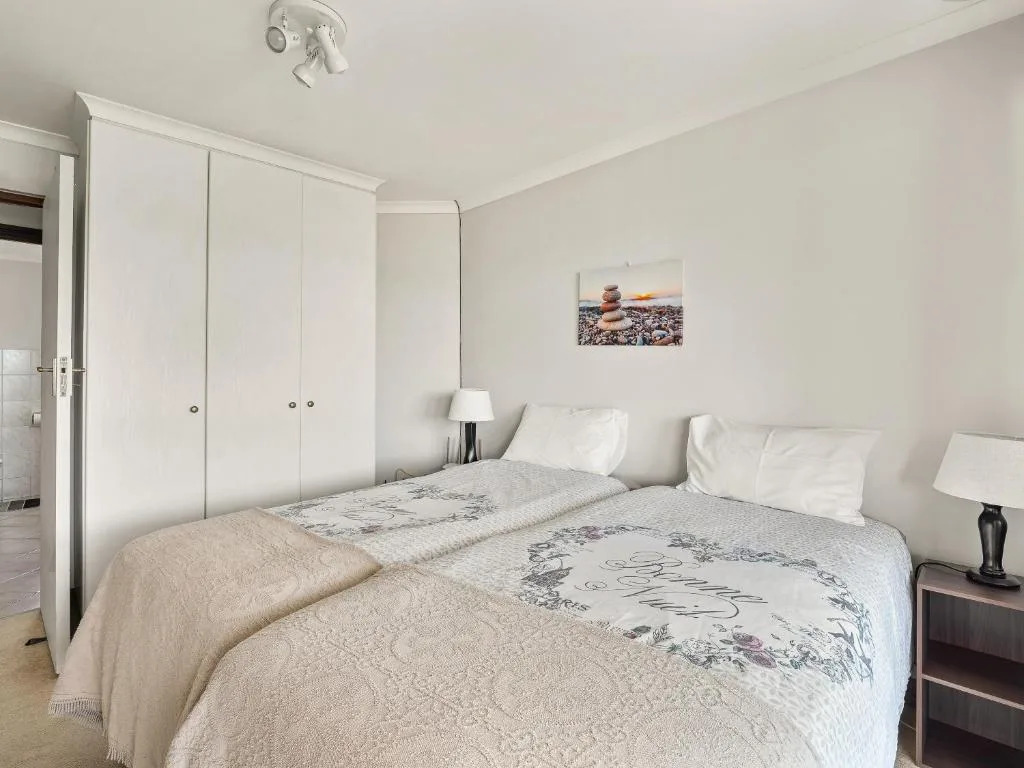 Bright bedroom with twin beds, white wardrobe, and coastal decor artwork