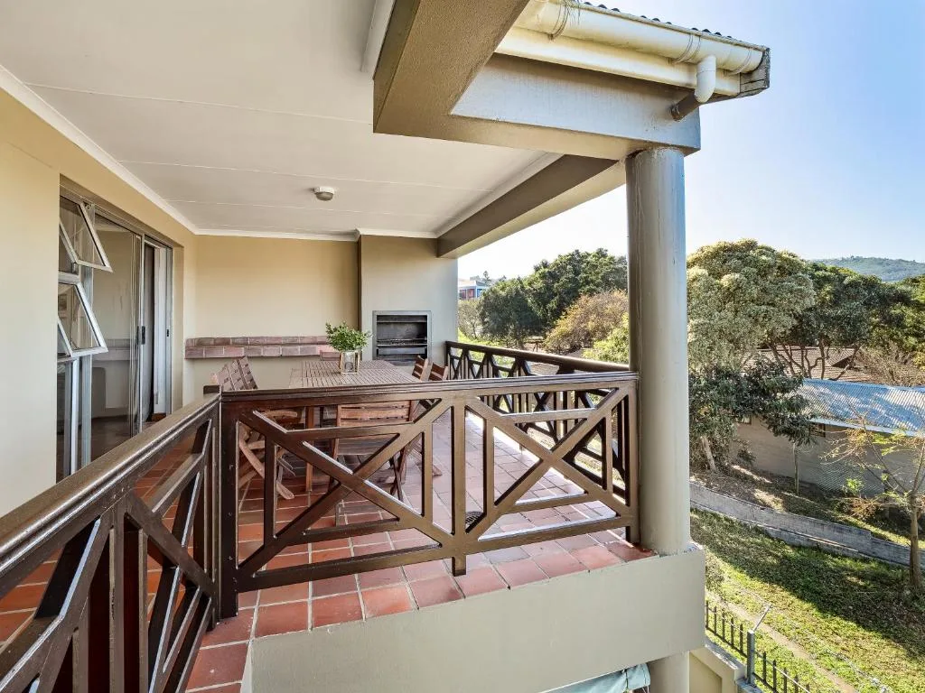 Covered balcony with wooden railings overlooking garden and hillside views