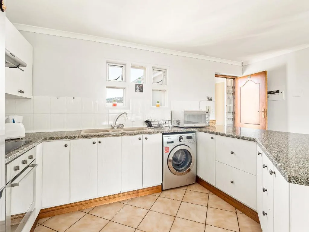 Bright white kitchen with granite countertops, washing machine, and wooden door entrance