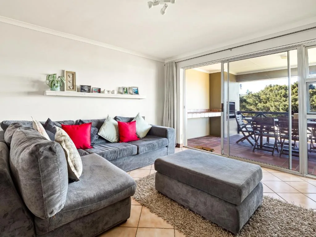 Modern lounge with gray sofa, red cushions, and sliding glass doors to deck