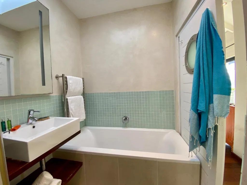 Modern bathroom with white sink, bathtub, green tile accents, and teal towels