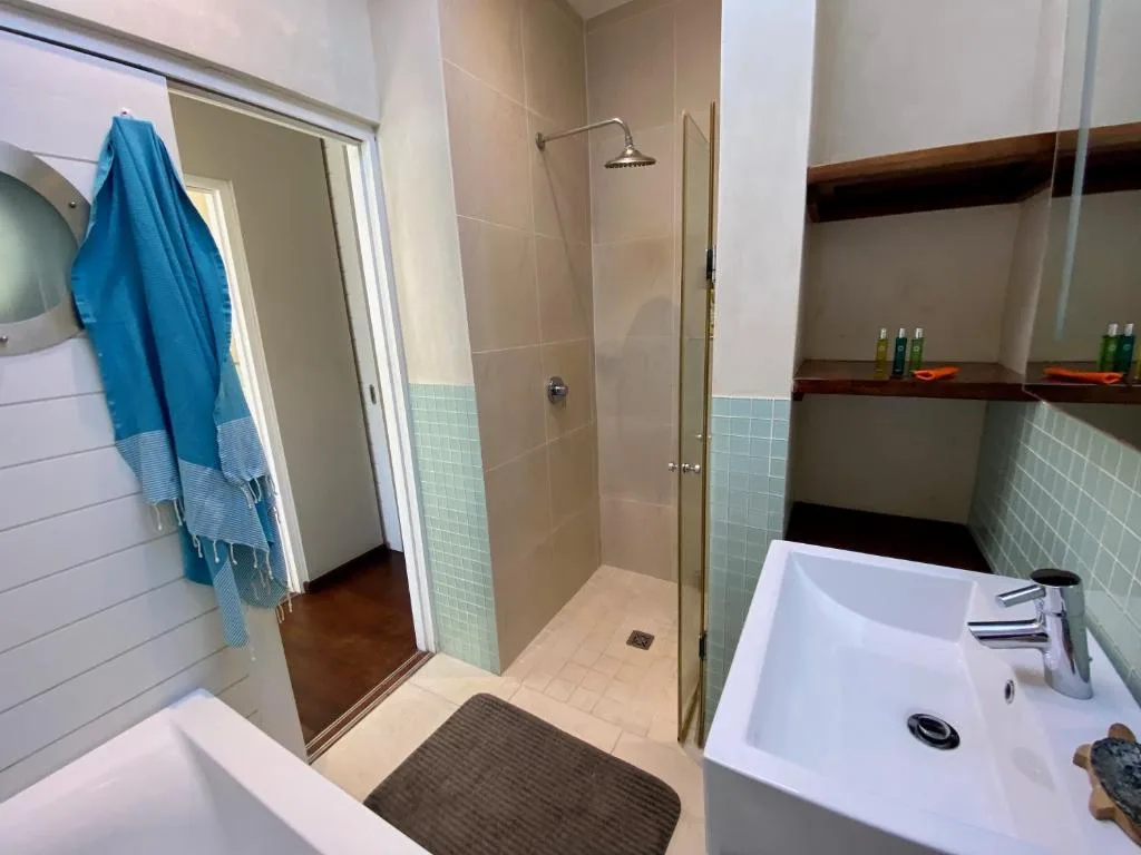 Modern bathroom with rainfall shower, white vanity sink, and blue towel
