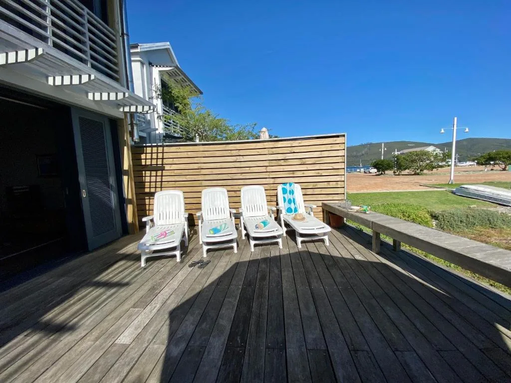 Wooden deck with four white loungers and wooden privacy fence