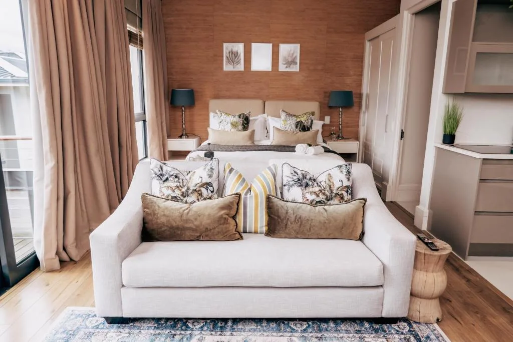 Spacious bedroom with cream sofa, king bed, warm wood accent wall, soft lighting