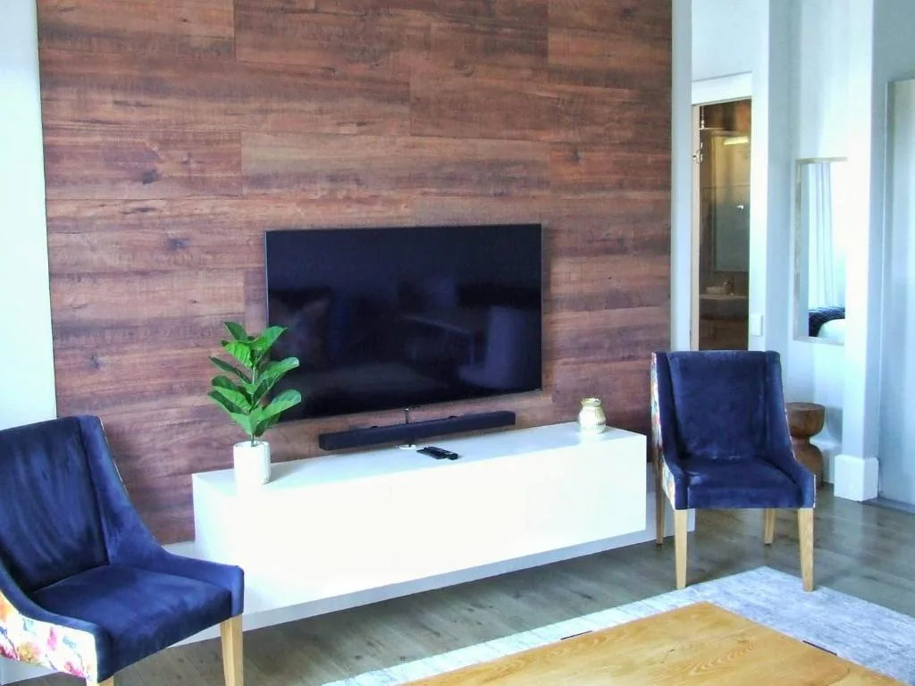 Modern living room with wall-mounted TV, wooden feature wall, blue velvet chairs