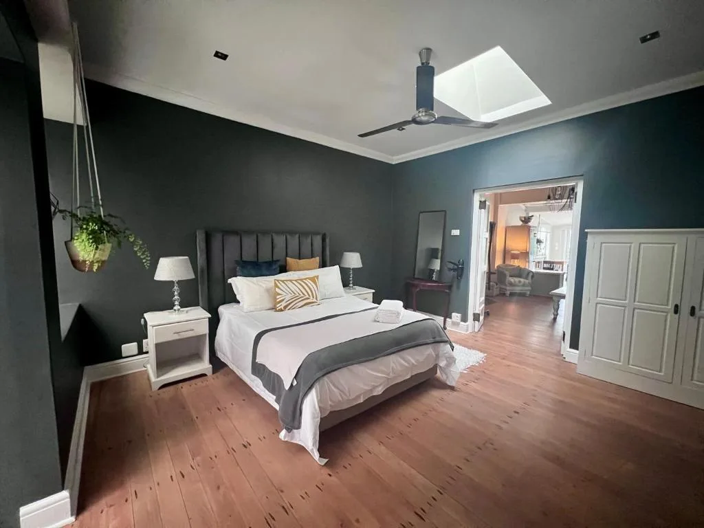 Spacious bedroom with queen bed, teal walls, skylight, and wooden floors