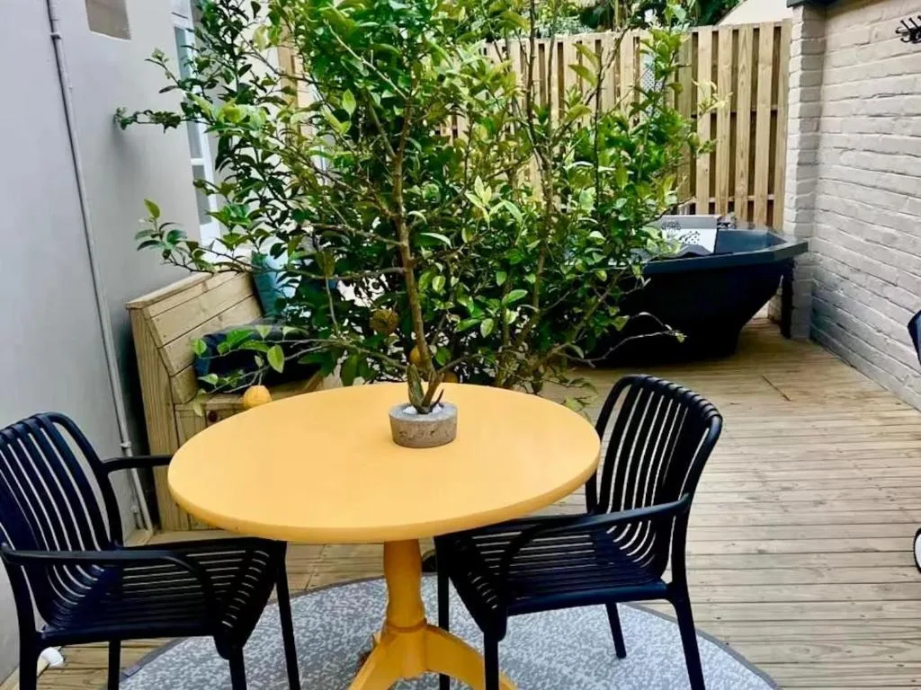 Outdoor patio with yellow round table, black chairs, lush greenery, wooden decking