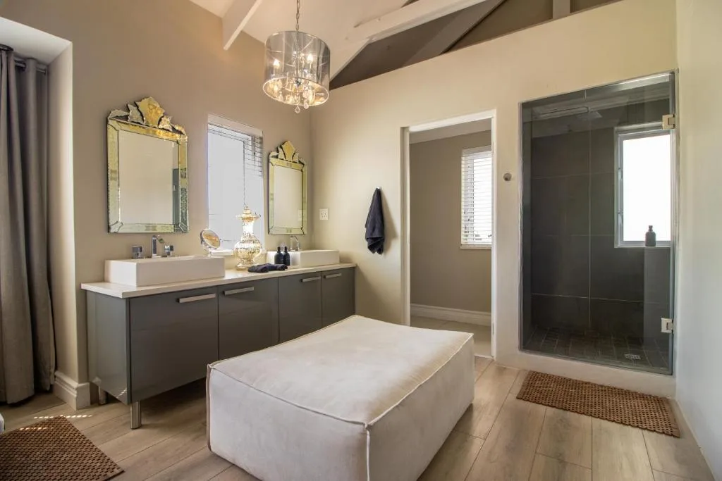 Modern bathroom with dark vanity, dual sinks, large mirrors, and glass shower enclosure