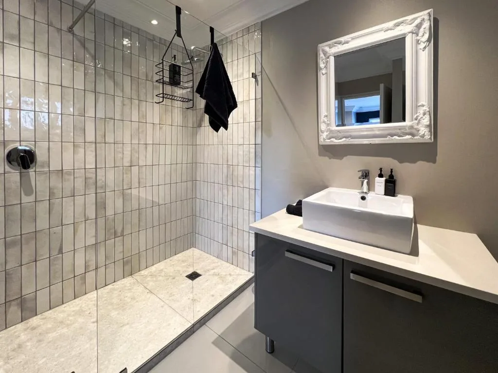 Modern bathroom with walk-in shower, white vessel sink, and decorative mirror