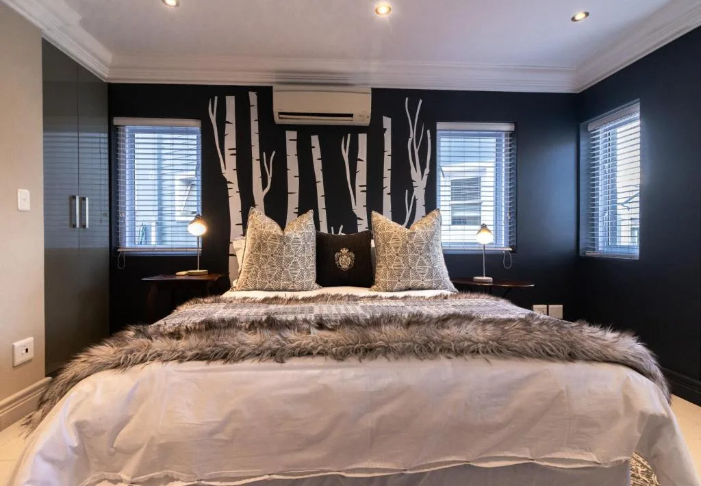 Modern bedroom with black accent wall, artistic tree mural, and luxury bedding