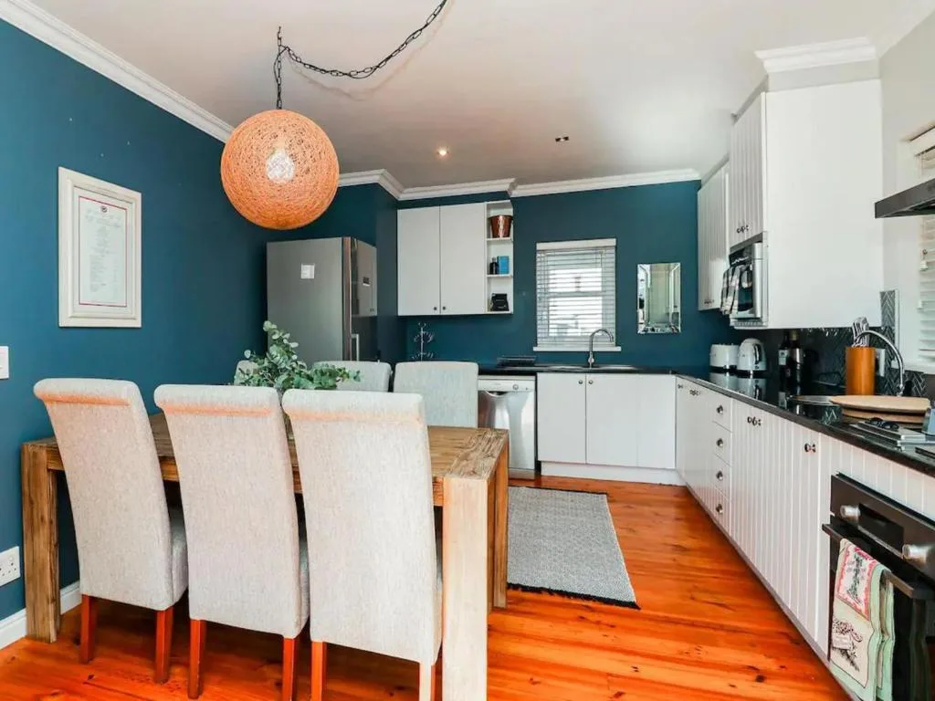 Modern kitchen with teal walls, white cabinetry, and dining area with wooden table