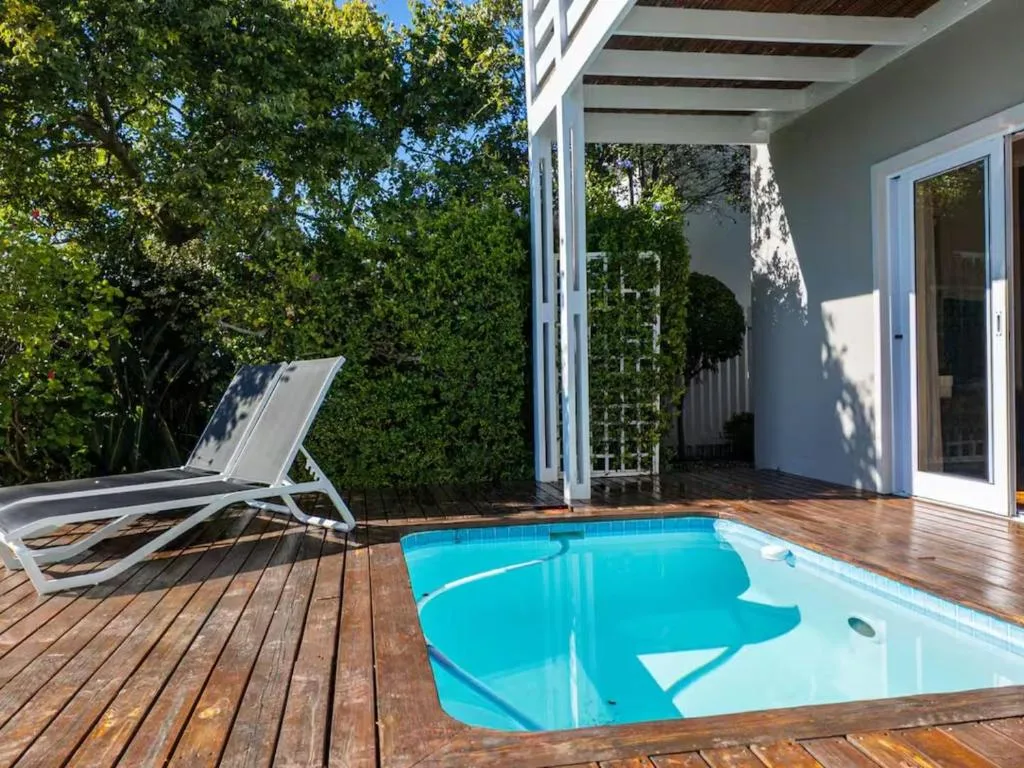 Bright blue swimming pool on wooden deck with lounger and pergola