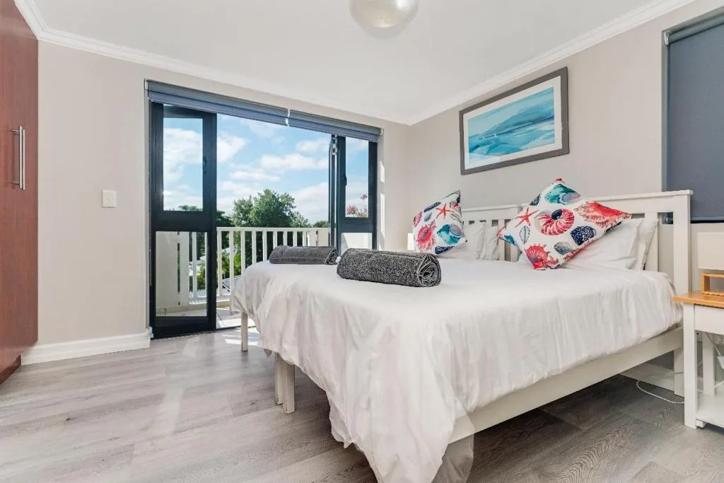 Bright bedroom with white bed, colorful pillows, and sliding doors opening to deck