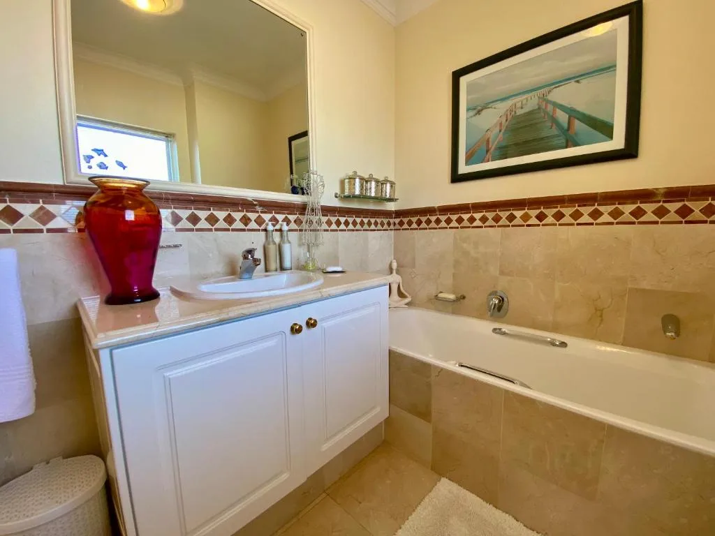 Elegant bathroom with white vanity, mirror, and soaking bathtub with tile surround