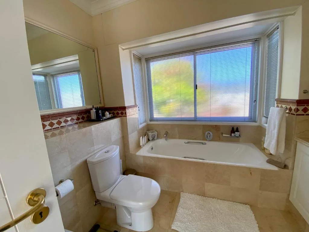 Spacious bathroom with bathtub, toilet, vanity mirror, and large windows