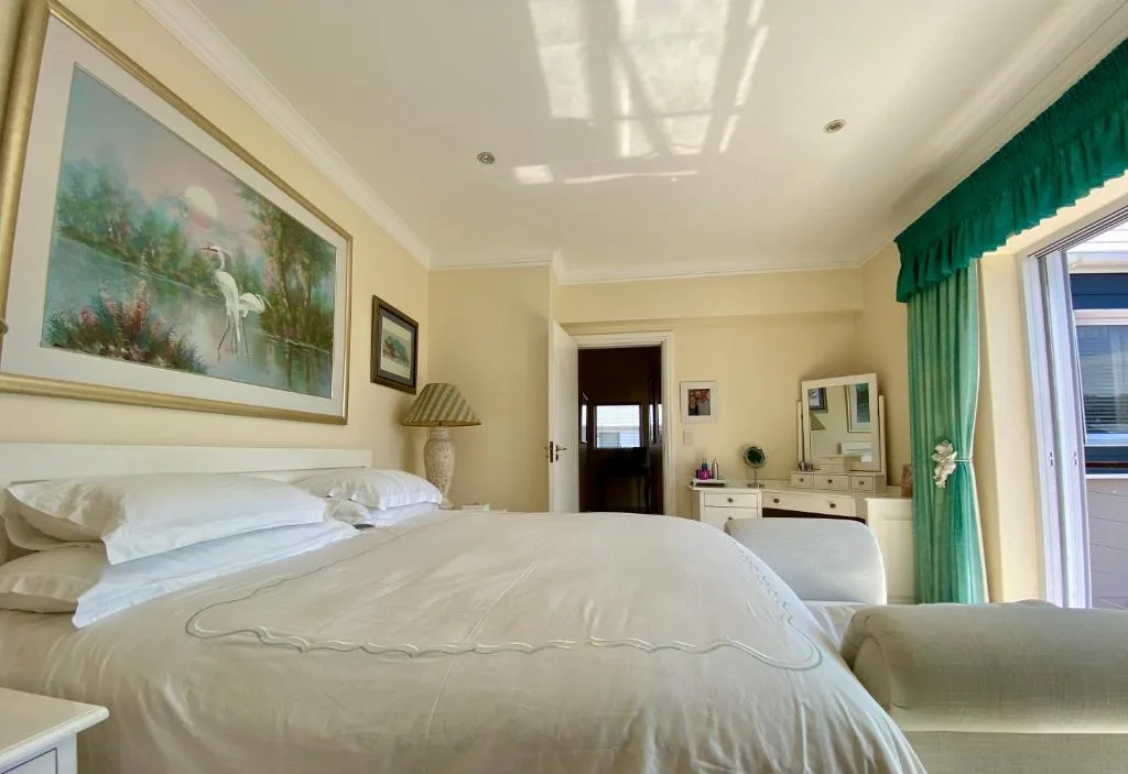 Bright bedroom with queen bed, cream linens, and green curtained door to deck