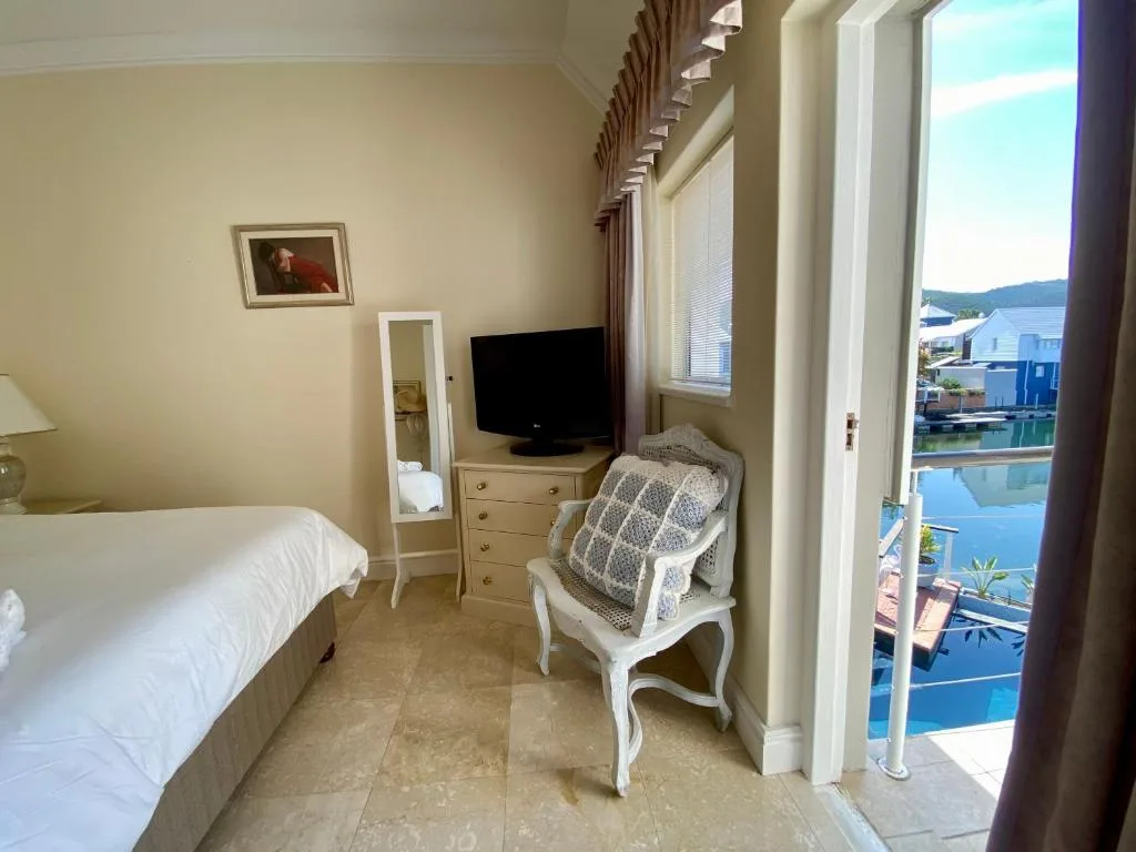 Bright bedroom with white bed, TV, chair, and waterfront views through glass doors