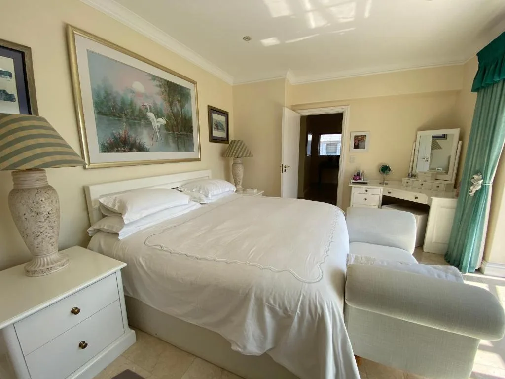 Bright bedroom with queen bed, white linens, vanity mirror, and artwork