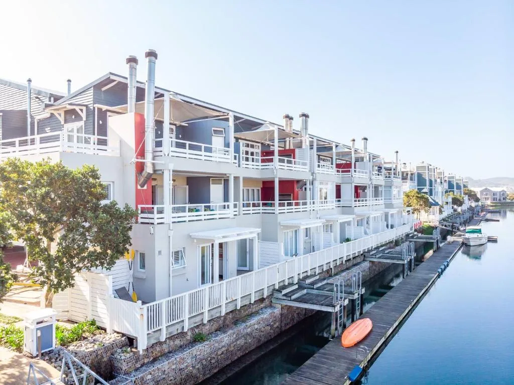 Modern waterfront apartment building with white railings and red accents on canal