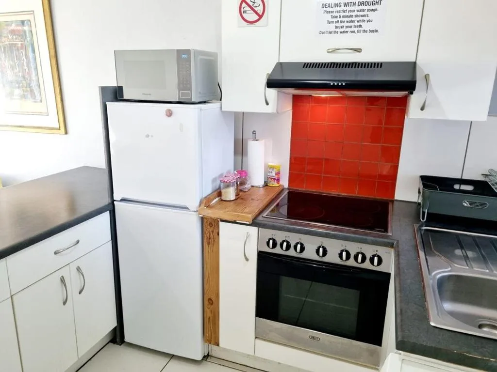Compact kitchen with white fridge, electric stove, and red backsplash tiles