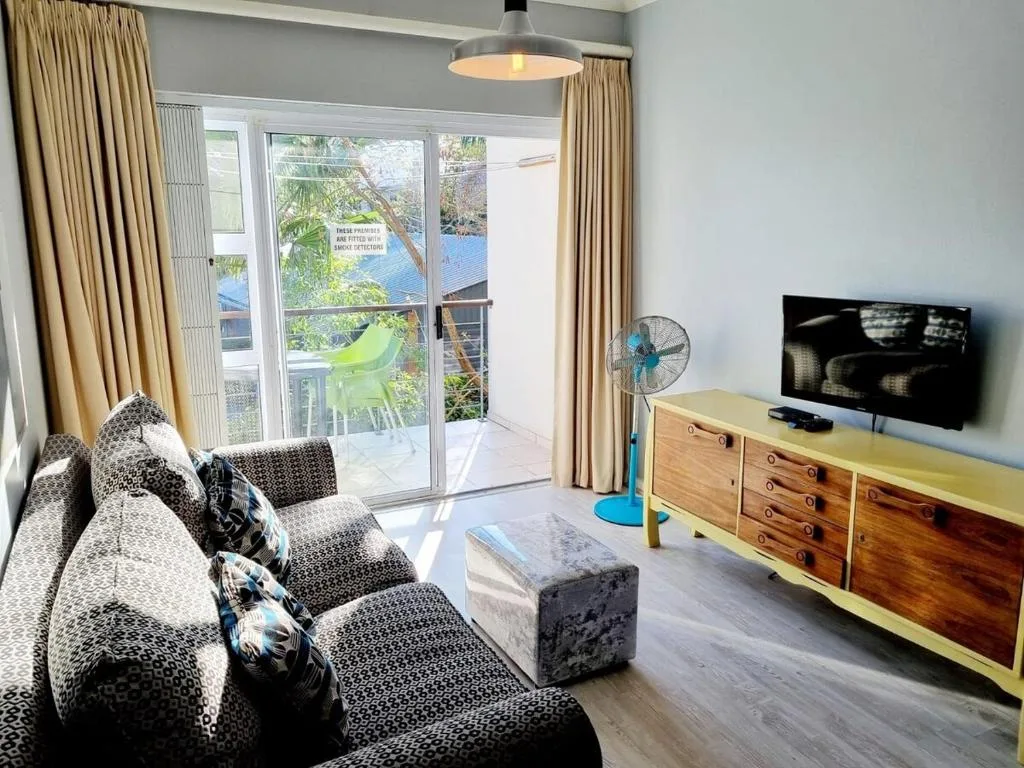 Modern living room with patterned sofa, TV unit, and lagoon views through glass doors