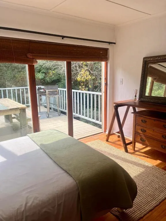 Bright bedroom with bed, wooden dresser, and glass doors opening to deck