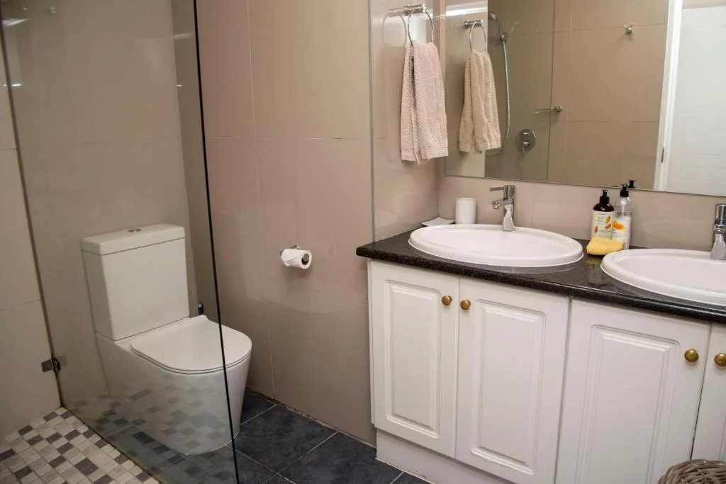 Modern bathroom with dual sink vanity, toilet, and glass shower enclosure