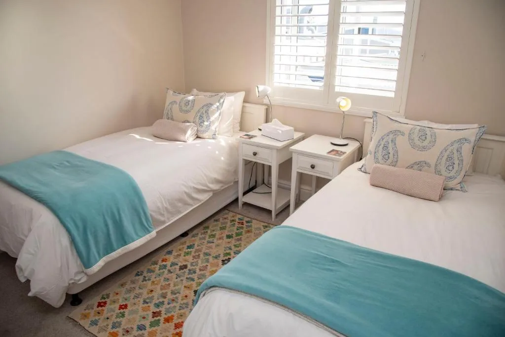 Bright bedroom with two single beds, decorative pillows, turquoise throws, and shuttered windows