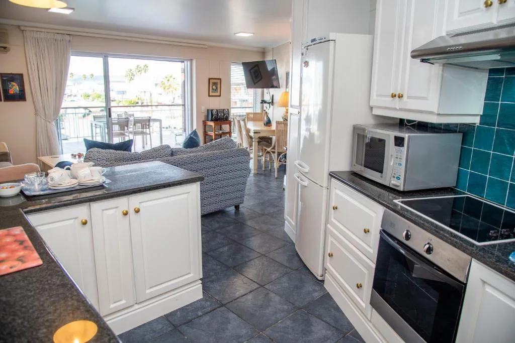 Modern kitchen with white cabinetry, teal tile backsplash, and open-plan living area