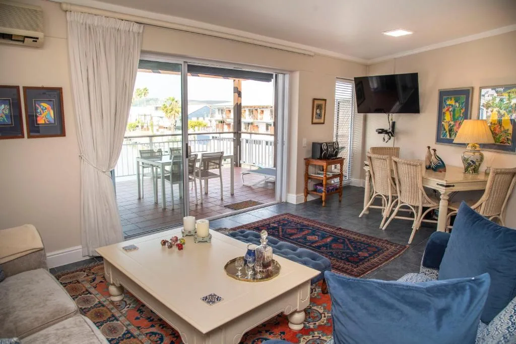 Open-plan lounge with blue sofa, white coffee table, deck access overlooking Knysna waterfront