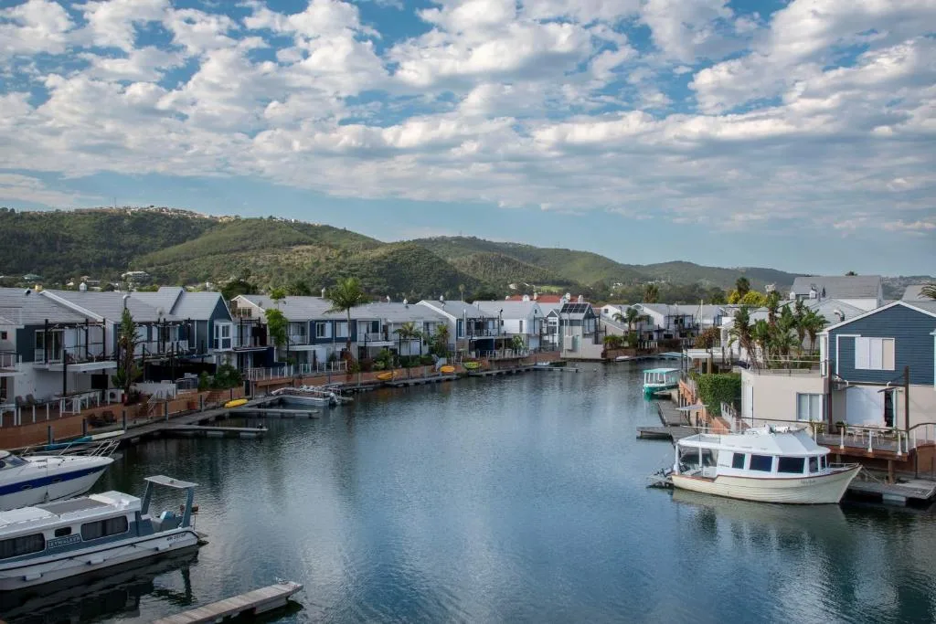 Waterfront homes with boats moored in calm lagoon water and green hills beyond