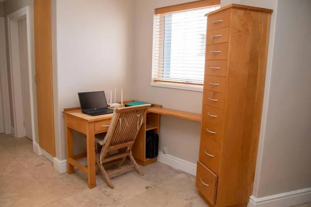Bedroom workspace with wooden desk, chair, and tall chest of drawers