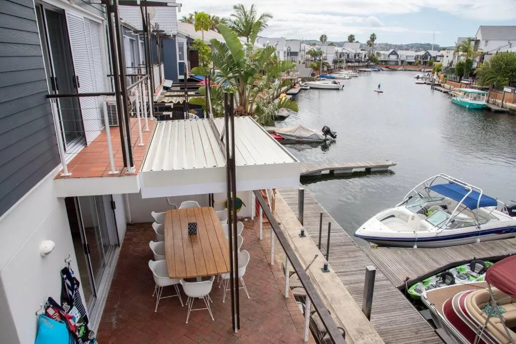 Waterfront deck with dining table, palm tree, lagoon views and moored boats