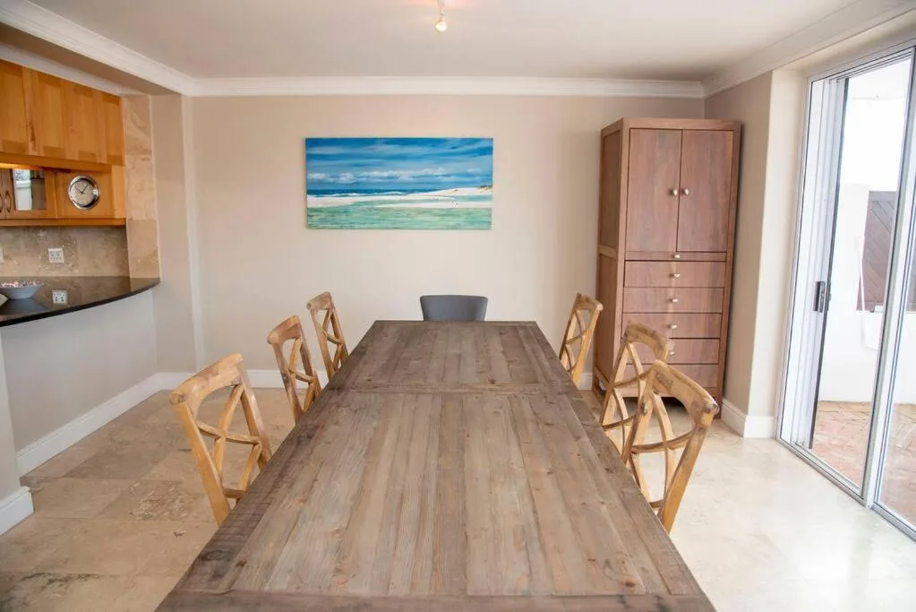 Spacious dining room with long wooden table and six chairs, beach artwork
