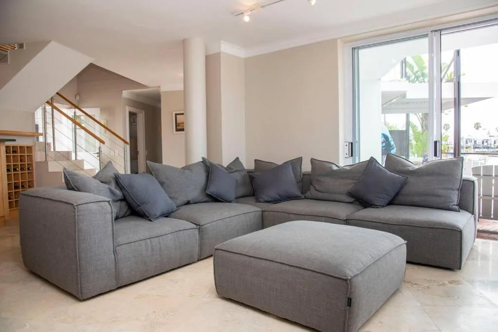 Spacious living room with gray sectional sofa and ottoman, bright windows overlooking water