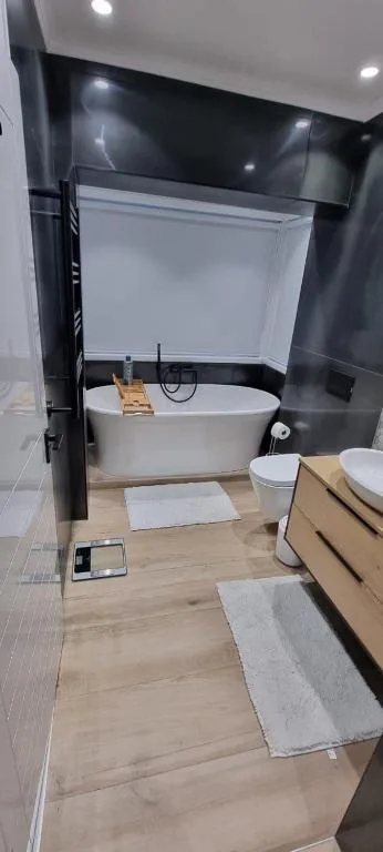Modern bathroom with freestanding tub, wooden vanity, and dark tile walls