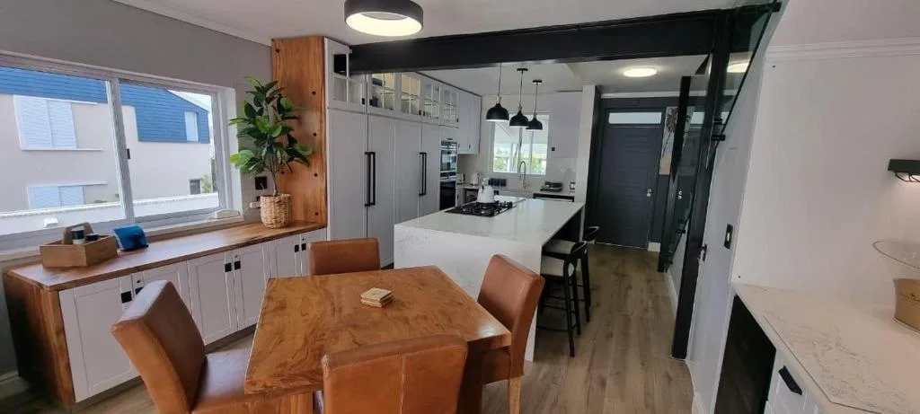 Modern dining area with wooden table and leather chairs, open-plan kitchen visible