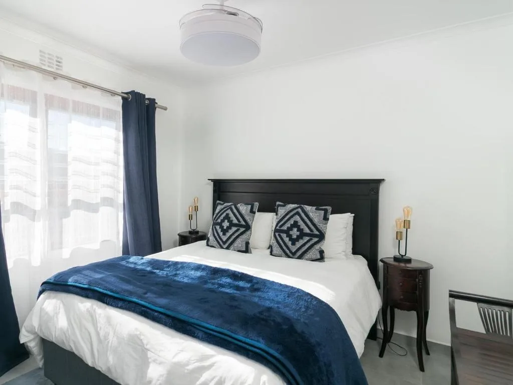 Bright bedroom with black headboard, white linens, blue throw, patterned cushions