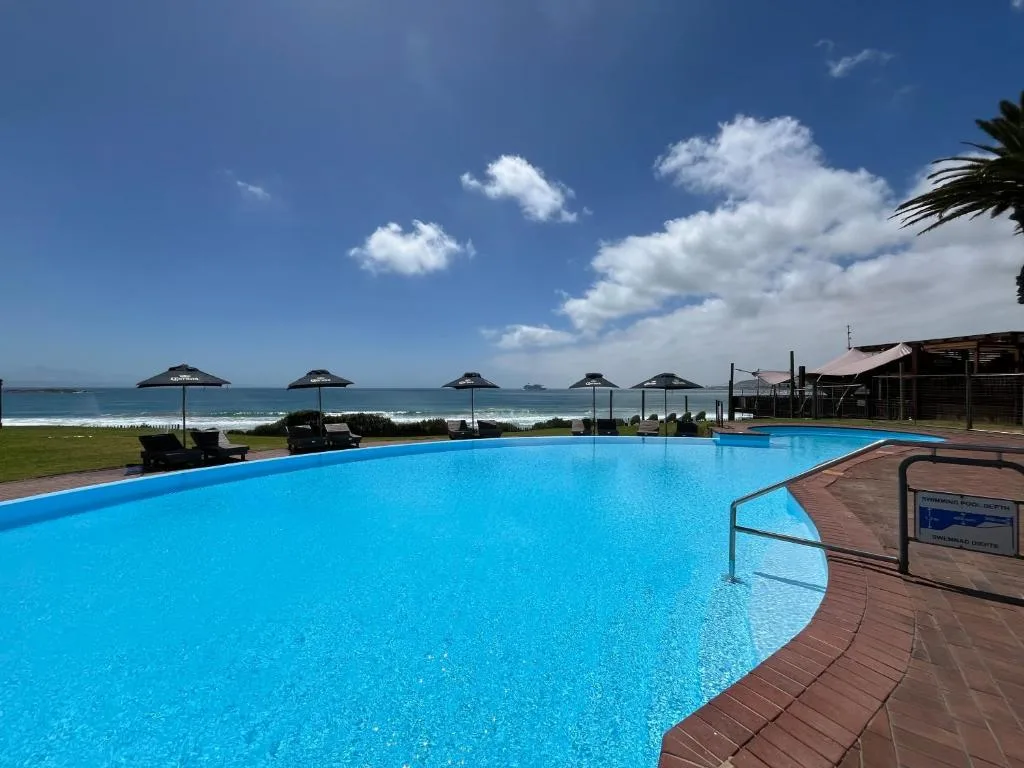 Sparkling blue swimming pool overlooking ocean beach with umbrellas and loungers