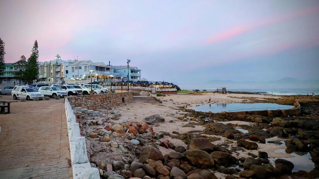 Beachfront property with colorful Victorian-style buildings and rocky shore at sunset