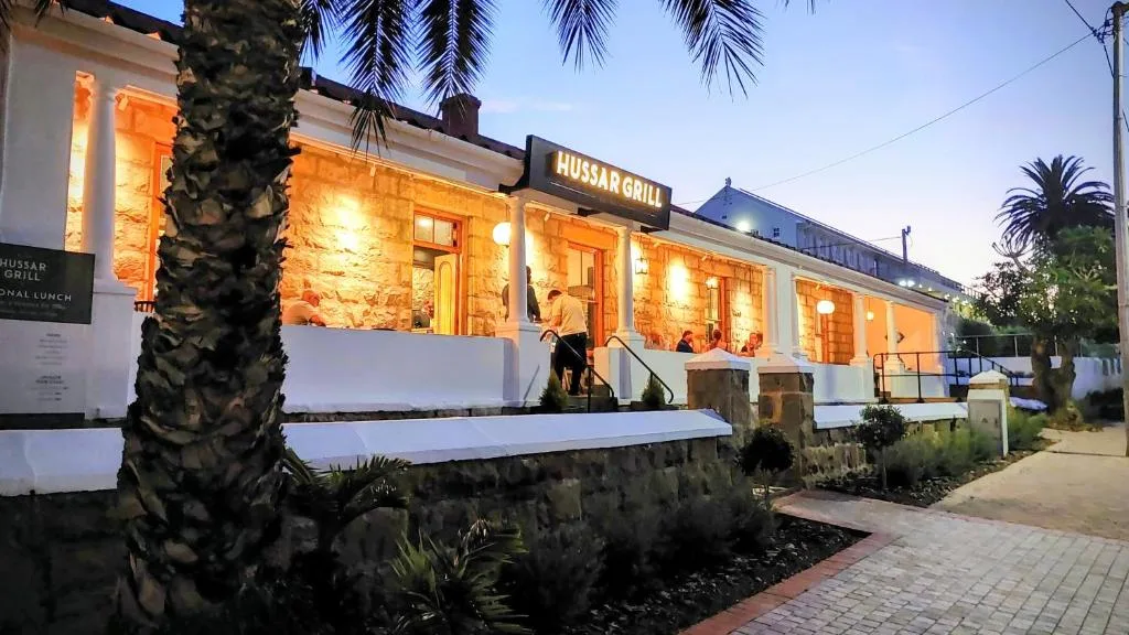 White cottage facade with illuminated windows and palm trees at dusk