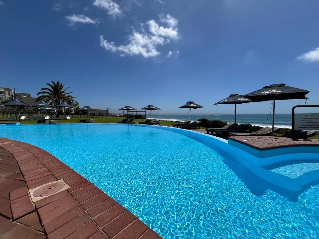 Large resort pool with ocean views, umbrellas, and coastal landscape