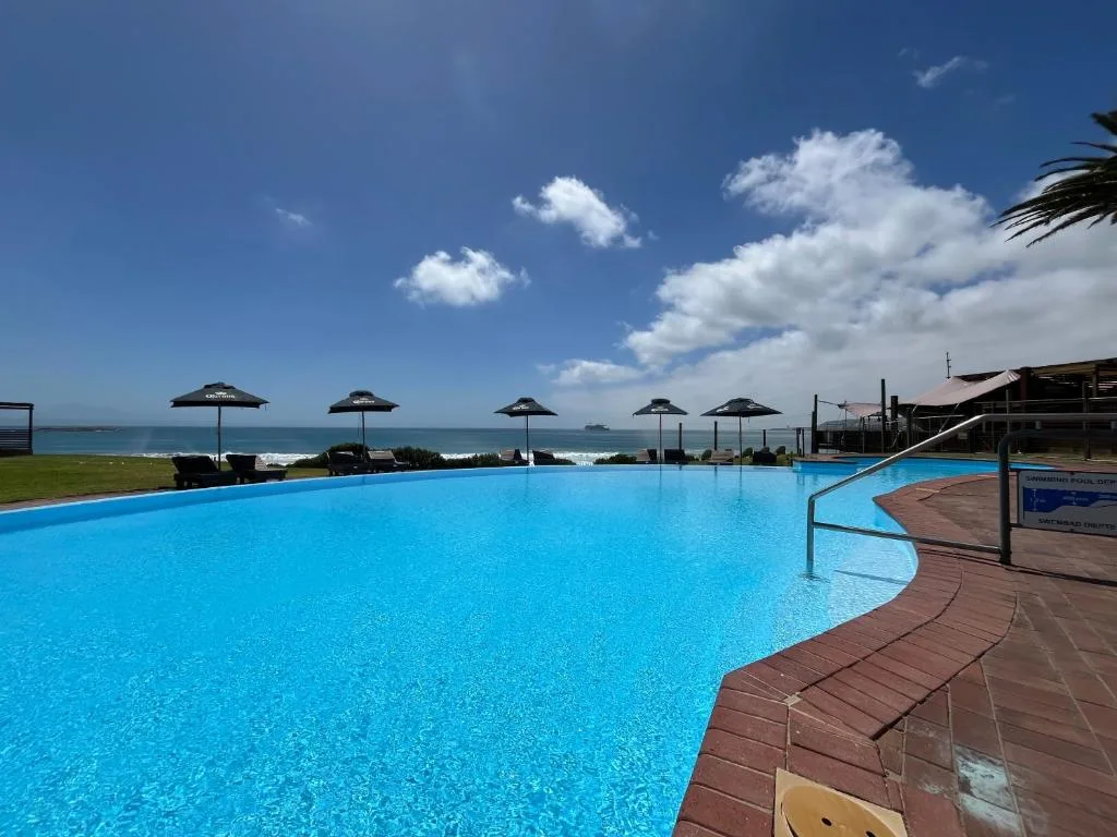 Resort swimming pool with ocean view and black umbrellas, coastal setting